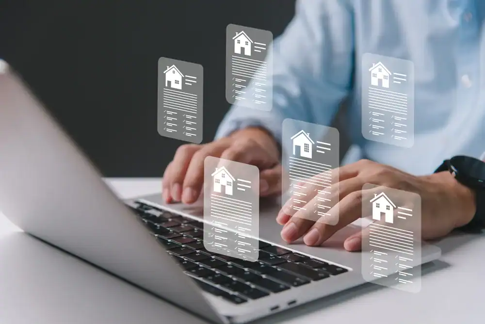 A person typing on a laptop keyboard with illustrated digital documents featuring house icons floating above the keyboard, representing online real estate, property management, and services like auto insurance Orange County.